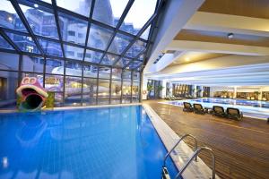 a swimming pool in a building with a large window at Limak Lara Deluxe Hotel & Resort Antalya in Lara