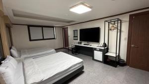 a bedroom with a bed and a desk with a television at Donghae Gloria Tourist Hotel in Donghae