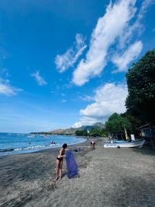 a woman standing on a beach with a towel at Putu Guest House Pemuteran in Pemuteran