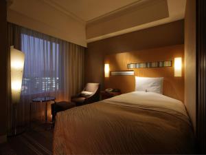 a hotel room with a bed and a chair and a window at Hotel Okura Fukuoka in Fukuoka