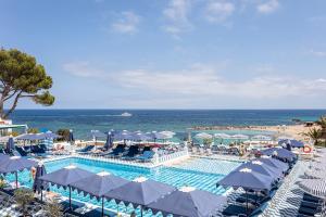 a swimming pool with blue and white umbrellas and the ocean at Hotel Mongibello Ibiza in Santa Eularia des Riu