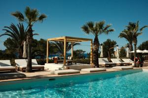 a swimming pool with lounge chairs and palm trees at Petunia Ibiza, a Beaumier hotel in Cala Vadella