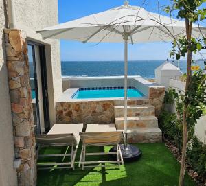 a patio with two chairs and an umbrella and a swimming pool at Esplanade Hermanus in Hermanus