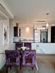 une cuisine avec des chaises violettes et une table en verre dans l'établissement Manhattan by Smart City Stays, au Cap
