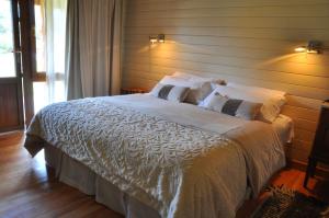 - une chambre dotée d'un grand lit avec des draps et des oreillers blancs dans l'établissement Hosteria Ruca Kitai, à Villa Lago Rivadavia