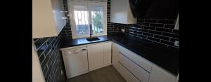 una cocina con armarios blancos y una pared de azulejos negros en Cozy Duplex Niza Beach, en Torre del Mar