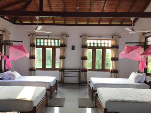 Habitación con 4 camas, sábanas rosas y ventanas. en Aki Villa en Pasikuda