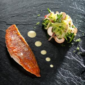 a black plate with a piece of fish and a salad at Logis Hotel Restaurant Nougier in Saint-Étienne-de-Fursac