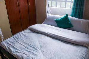 a bed with white sheets and a green pillow at Eagles one bedroom in Kisii CBD with Balcony in Kisii