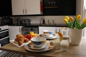 a kitchen table with croissants and cups and plates of food at Top Spot 2-Bed Spacious Apartment Town Centre Train Station WIFI in Colchester