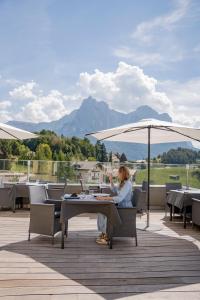 a woman sitting at a table under an umbrella at Hotel Alpenflora in Castelrotto