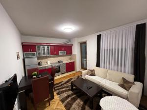 a living room with a couch and a kitchen with red cabinets at Feti’s cozy apartment near the park city in Prishtinë