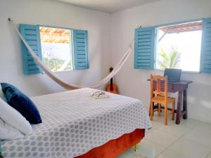 um quarto com uma cama de rede de descanso, uma secretária e 2 janelas em Casinha Estrela do Mar o Oceano aos seus Pés em Aracati