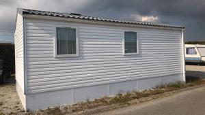 a white building with two windows on the side of it at Mobil Home in Siouville