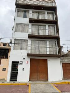 a tall white building with two brown doors at Paris Senlis Hostel Plus in Chimbote