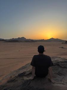 Um homem sentado no deserto a ver o pôr-do-sol. em Dream Bedouin life camp em Wadi Rum