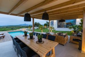 patio con mesa de madera, sillas y piscina en Petra Luxury Villa, en Heraclión
