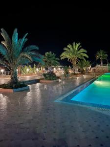 una piscina por la noche con palmeras y sillas en L'oliveraie D'amizmiz, en Amizmiz