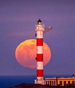 un faro rosso e bianco con la luna sullo sfondo di Casa Dora: Tradicional y al borde del mar. a Poris de Abona