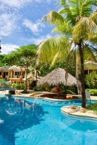 a swimming pool with a straw umbrella and palm trees at Cocomarindo Breeze Condo And Amazing Pool in Coco
