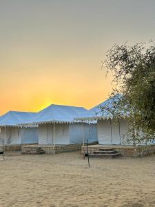 una fila de tiendas blancas en una playa con puesta de sol en Jaisan Boutique Desert Camp Jaisalmer, en Jaisalmer
