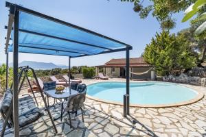 梅加尼西岛Villa Jimmy's Katomeri 3的泳池上方有一个蓝色的天篷，上面有一张桌子和几把椅子