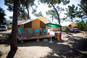 une petite tente jaune avec des chaises et un parasol vert dans l'établissement Huttopia Noirmoutier, à Noirmoutier-en-l'lle