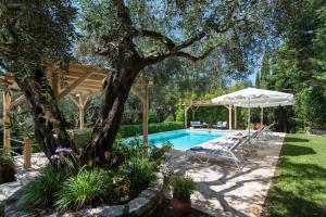 a pool in a backyard with a tree and an umbrella at Villa Apleton in Kassiopi