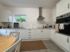 una cocina con armarios blancos y una mesa. en Charming 2BR Cottage - Fully Furnished - 10min LGW - Free Parking, en Crawley