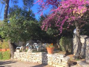 un jardin avec un mur en pierre et un arbre avec des fleurs roses dans l'établissement Appartements avec jardin dans Villa Rocaille, à Cassis