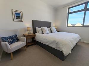 a bedroom with a bed and a chair and a window at Courtside Views Empire Apartment in Muizenberg
