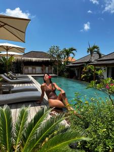 a woman in a bikini sitting next to a swimming pool at EHOA BALI Nyanyi Boutique Hotel - In front of entrance to NUANU in Tanah Lot