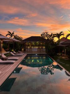 a swimming pool with lounge chairs and a sunset at EHOA BALI Nyanyi Boutique Hotel - In front of entrance to NUANU in Tanah Lot