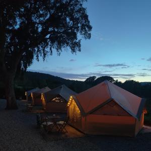 Camping Pla de la Torre في سان أنتوني دي كالونخي: صف من الخيام تجلس تحت شجرة في الليل