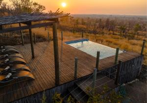 a wooden deck with a swimming pool and a sunset at Hideaways Nantwich Lodge, Hwange in Hwange