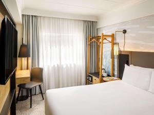 ベッドフォードにあるMercure Bedford Centre Hotelの白いベッドとデスクが備わるホテルルームです。