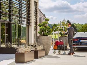 un hombre empujando un carro de equipaje delante de un edificio en Le Domaine des Vanneaux Golf et Spa Mgallery, en LʼIsle-Adam