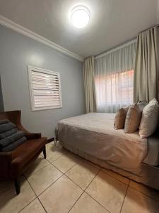 a bedroom with a bed and a chair and a window at Bluestream Villas in Pretoria