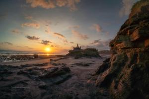 a sunset over a beach with a castle on a cliff at Pondok Dauh Ancak in Tabanan