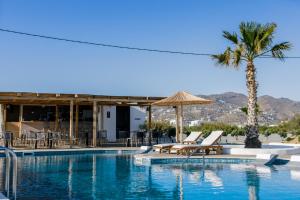 a swimming pool with two lounge chairs and a palm tree at Naxos Finest Hotel & Villas in Naxos Chora