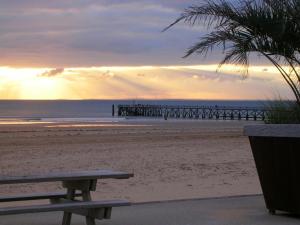 a bench on the beach with a pier in the background at L'Entre Vagues in Saint-Jean-de-Monts