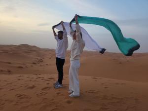 zwei Menschen, die in der Wüste stehen und eine Fahne halten in der Unterkunft RiadSuerteloca Merzouga in Merzouga