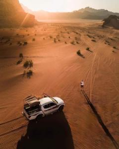 Un uomo in piedi accanto a un'auto bianca nel deserto. di Bedouin bunch camp a Wadi Rum