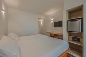 Costa Nova Hotel في كوستا نوفا: غرفة نوم بسرير ابيض وتلفزيون