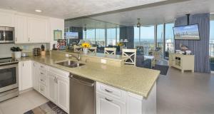 a kitchen with white cabinets and a view of a living room at Ocean Condo 104 ~ Ground Floor Corner Condo with wrap around balcony Walk right out to Pool in New Smyrna Beach