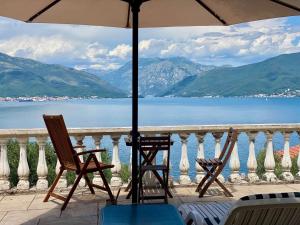 2 Stühle und ein Sonnenschirm auf einem Balkon mit Blick auf das Wasser in der Unterkunft Villa Miran Boka Bay in Krasići