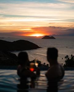 dos personas sentadas en el borde de una piscina viendo la puesta de sol en Buzios Mar Hotel & Spa, en Búzios