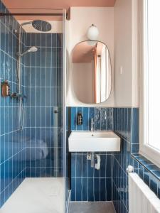 La salle de bains est pourvue de carrelage bleu, d'un lavabo et d'une douche. dans l'établissement Hôtel Biskui, à Levallois-Perret