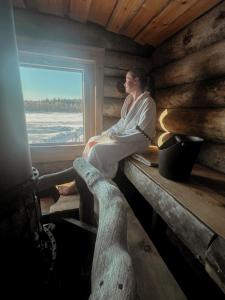 a woman sitting in a cabin looking out the window at Villa Karhukumpu in Ivalo