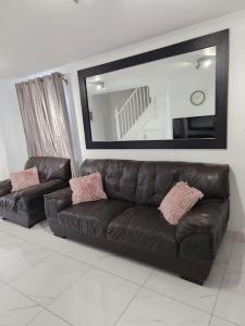 a black leather couch in a living room with a mirror at Luxurious 2 Bedroom House With Garden And Free Parking in Thamesmead